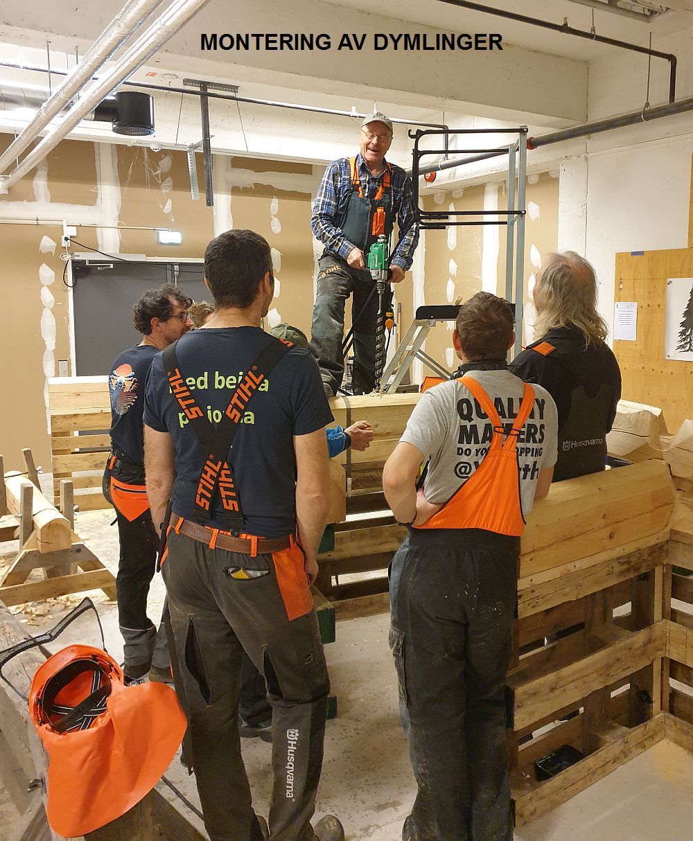 George står på laftet og borer for dymlinger mens deltakerne ser på.